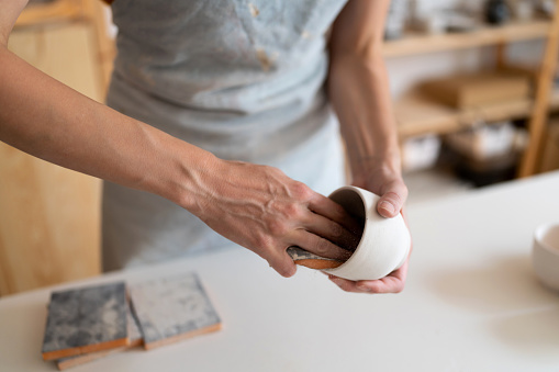 Unecognizable female potter, using sandpaper to polish the pottery