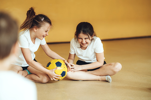 Young school children having fun with ball at gym