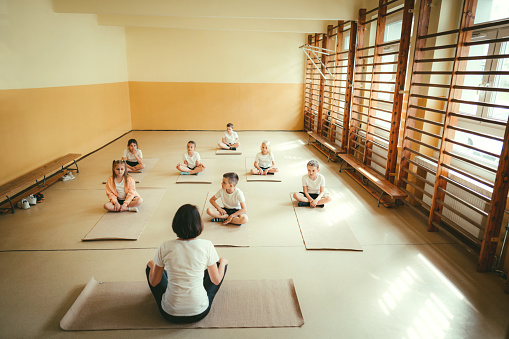 Rear view of teacher teaching yoga to students during physical education class