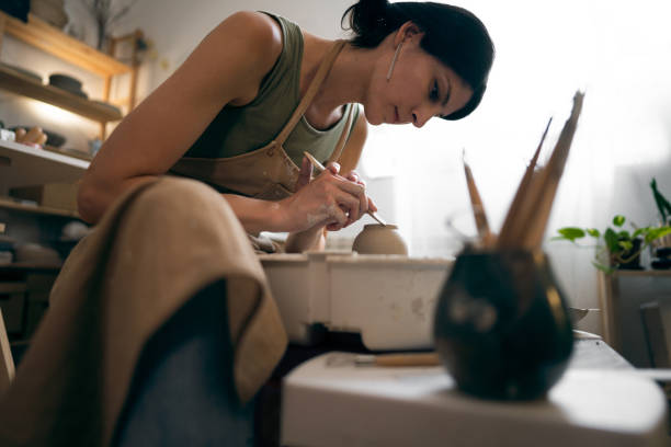 Female ceramics maker or potter working with pottery wheel in workshop.