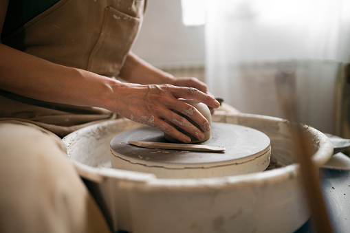 Unrecognizable female ceramics maker or potter working with pottery wheel in workshop.