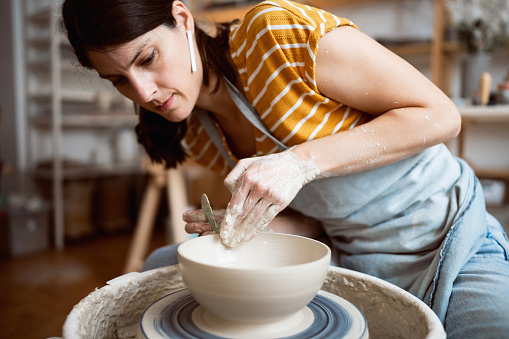 Caucasian female potter, working on pottery wheel, at her modern workshop