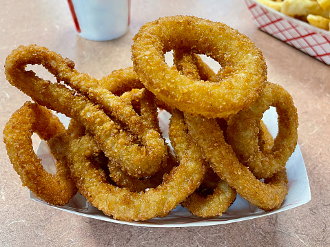 A freshly made serving of deep-friend onion rings at a restaurant with a side of waffle-cut French fries and a drink.
