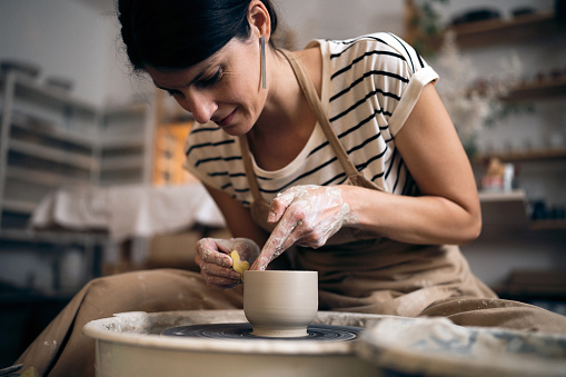 Woman molding clay pot with a sponge