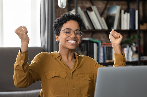 African woman sit at desk with laptop celebrate great news