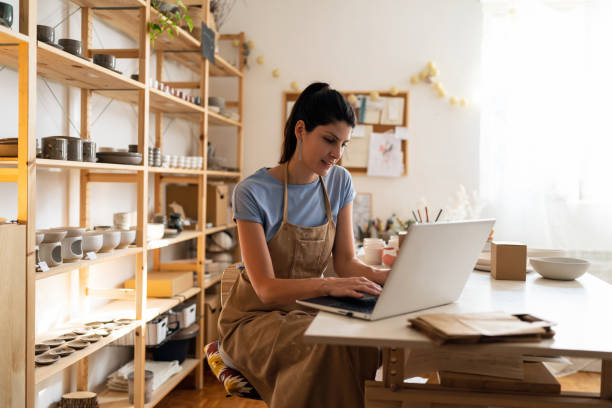 istock Female small business owner working on laptop from her modern pottery studio 1411275833
