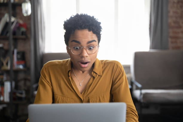Surprised African woman gawp at laptop with mouth opened Surprised African woman gawp at laptop screen with big eyes and opened mouth cant believe in luck, lottery win, read unbelievable news, get fantastic commercial offer, sell-out, huge discounts concept gawp stock pictures, royalty-free photos & images