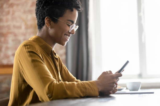 istock Smiling African woman in eyeglasses sit at table using smartphone 1411275957