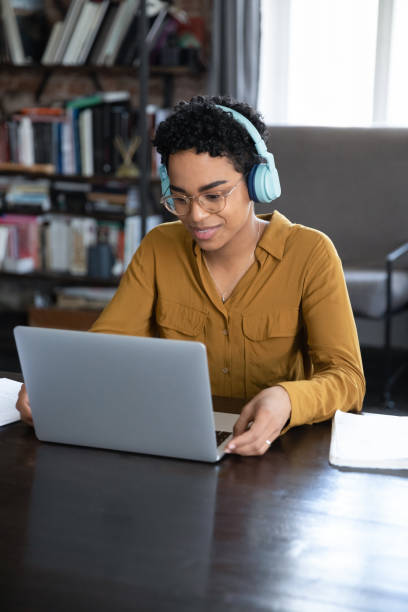 donna africana che studia usando il laptop, ascolta il corso audio attraverso le cuffie - secret identity audio foto e immagini stock