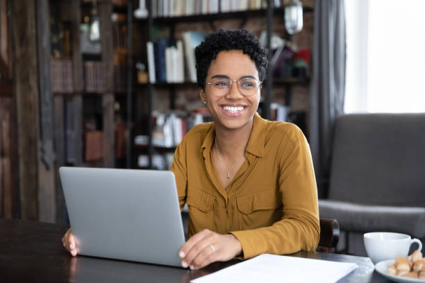 African woman distracted from working on laptop looks into distance stock photo