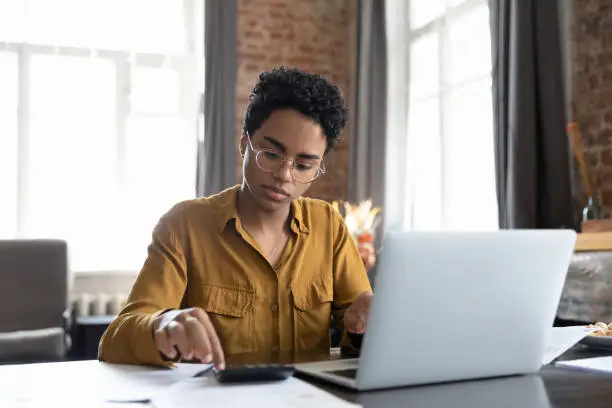 Photo of African woman sit at desk calculates bills do accountancy job