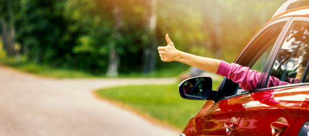woman inside car on the road with thumb up gesture out of the window. banner with copy space stock photo