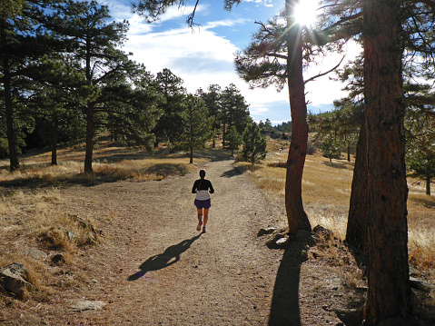 During a fall morning, a woman trail runner in a long sleeve shirt and shorts runs along the Castle Trail on Mount Falcon in the Colorado Rocky Mountain Front Range.