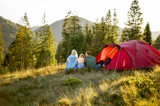 Family with a kid enjoy great view on mountains while sit together at campsite near the tent. Family trip on nature concept