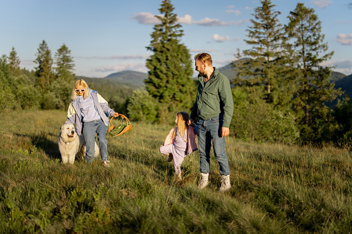 Young caucasian couple with little girl and dog have fun spending leisure time together on nature. Happy family traveling in the mountains