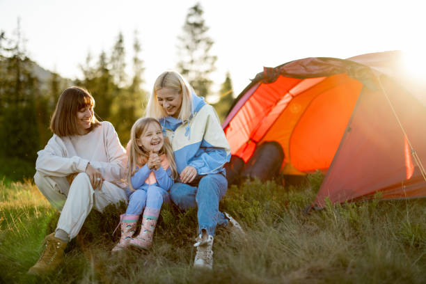 Two women sit with a little girl at campsite stock photo