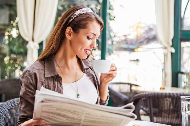 istock Happy young woman drinking coffee and reading newspaper 1411286341