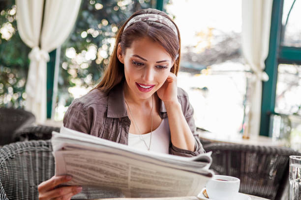 istock Young woman drinking coffee and reading newspaper at cafe 1411286348