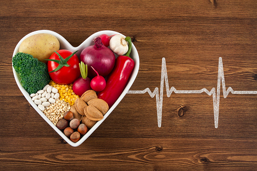Heart health concept with related foods in white heart shaped bowl. potato red peppers, broccoli, radish, red onion, garlic, dry beans, almonds, nuts, and other legumes were arranged in heart shape plate