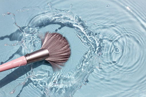 Makeup brush in clean water with a splash. Summer cosmetics concept. Top view.