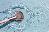 Makeup brush in clean water with a splash. Summer cosmetics concept.