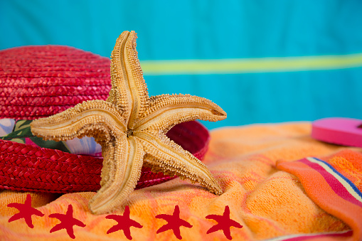 Summer vacation.  Beach towel with turquoise water look background.  Large starfish and other shells.  Red straw hat.