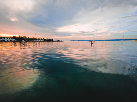 Colorful lake waters meet a dramatic cloudy sky at the horizon. Located within a bay of water with views of moored sailboats and the shoreline. Dawn or dusk dramatic landscape scene. Located on Little Traverse Bay in Harbor Springs, Michigan, USA.