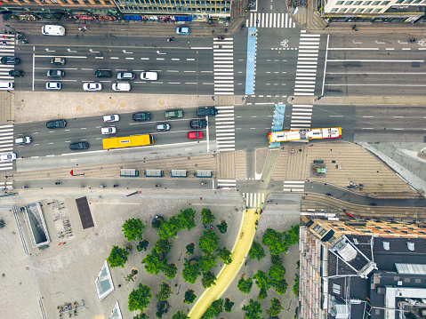 Top down drone image of bicycle and car traffic in central Copenhagen at the City Hall Square. The characteristic yellow, public busses are driven by electricity and bicyclist on bicycle lanes are dominating the commute. This smart city emphasises alternative and public transportation, and the area sports an urban forest supporting biodiversity.