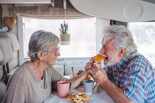 Beautiful happy caucasian senior couple in travel vacation leisure sitting inside a camper van dinette enjoying breakfast together