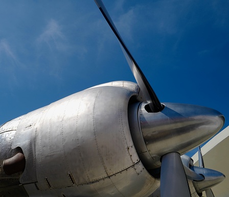 Close up of airplane turboprop engine with propeller, parts of aircraft fuselage, and cockpit on cloudy sky background