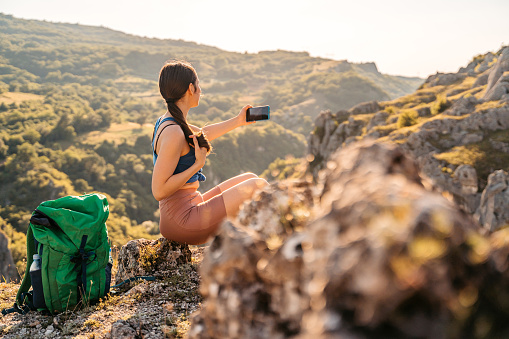 Beautiful young woman exploring nature, climbing on the mountain and taking a picture of the nature from the top.