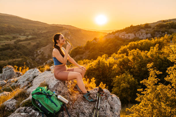 Beautiful young woman exploring nature, climbing on the mountain. Eating a protein bar after a hike, at the top of the mountain.
