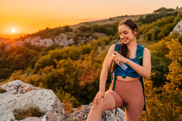 Young Woman Applying Mosquito Repellent On The Top Of The Mountain Beautiful young woman exploring nature, hiking on the mountain. Applying mosquito and bug repellent spray on the top of the mountain. backpack sprayer stock pictures, royalty-free photos & images