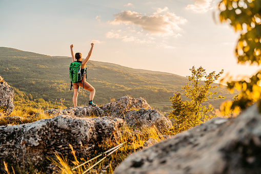 Beautiful young woman exploring nature, climbing on the mountain. Arms outstretched and cheering for the success after getting on the top of the mountain.
