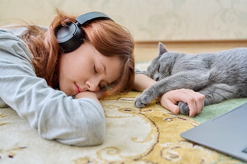 Preteen girl in headphones sleeping with cat on floor at home