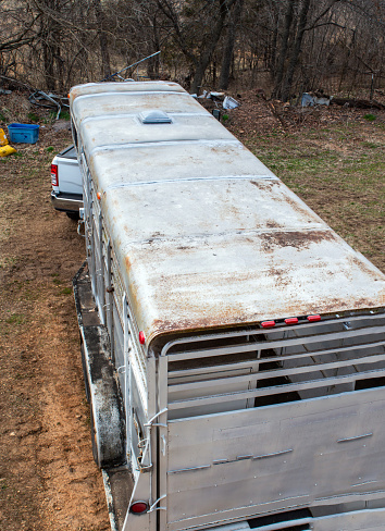 A silver colored stock trailer is parked and ready for loading. Looking down at the top of the trailer it appears it could use a fresh paint job.