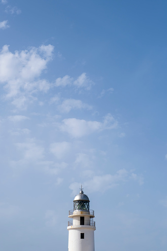 tip of a white lighthouse with a weather vane on the roof, a blue sky in the background with some clouds, Cavalleria lighthouse, Menorca, Spain, copy space