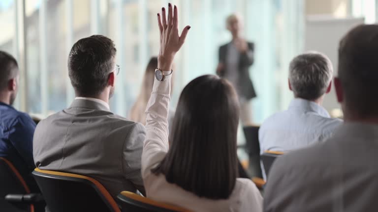 Woman raising her hand to ask a question at a seminar in a board room.