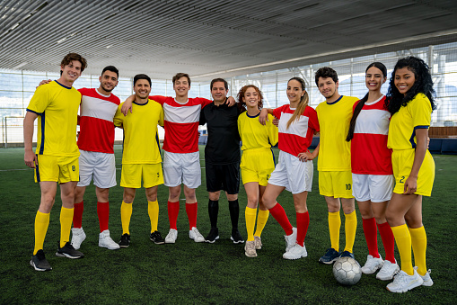 Happy co-ed soccer teams at the field with the referee and looking at the camera smiling - sports concepts