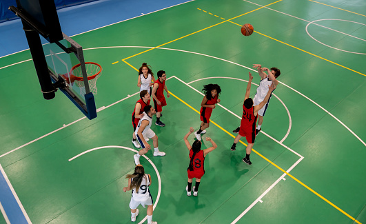Smiling female defending basketball from opponent. Teenage girls are playing match in court. They are in sports uniform.