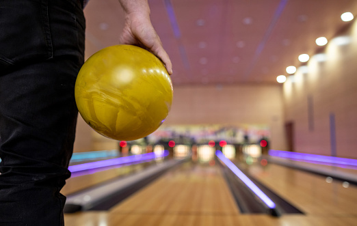 Close-up on a man bowling and holding a ball at the alley - sports and recreation concepts