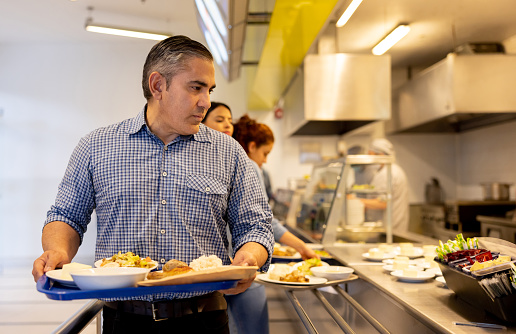Latin American man eating at a buffet style restaurant and holding his tray