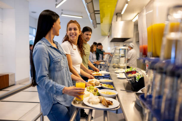 Happy women eating at a buffet style cafeteria Happy Latin American women eating at a buffet style cafeteria and holding their trays canteen stock pictures, royalty-free photos & images