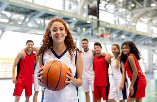 Portrait of a happy female player leading a basketball team and holding a ball while looking at the camera smiling - sports concepts