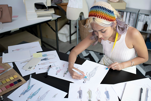 Attractive Asian woman fashion designer is drawing sketch and working in her studio. Asian woman tailor in seamstress studio.