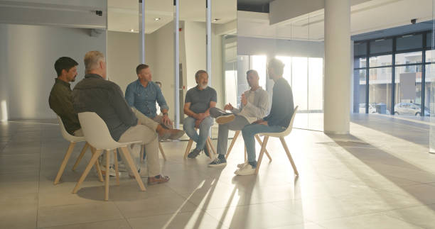 istock Group of men sitting in a circle during a therapy session. A psychology support group speaking about their emotions and mental health problems. Recovering addicts talk in a meeting at a rehab center 1411325440