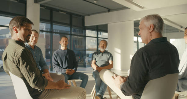 istock Group therapy session for support, mature men sitting in a circle with a therapist. Addicts at an AA meeting discussing personal problems or psychological struggles. Grief counselling for widowers 1411325468