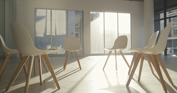 Circle of chairs in an empty room for group therapy session in a wellness or rehab center with sunshine in background. Large office space with no people prepared for team building exercise or meeting