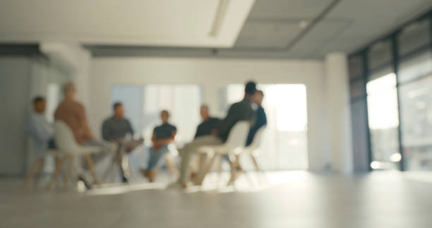 istock Businessmen sitting in a support therapy meeting with blur background and copy space. Corporate people in a circle, participating in an interactive group session or informal team building discussion 1411325480