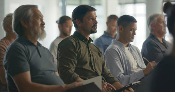 istock Group of business men sitting in an office conference room, developing skills and taking notes. Closeup of professional business people in seats attending a seminar or workshop to learn in an office 1411325530